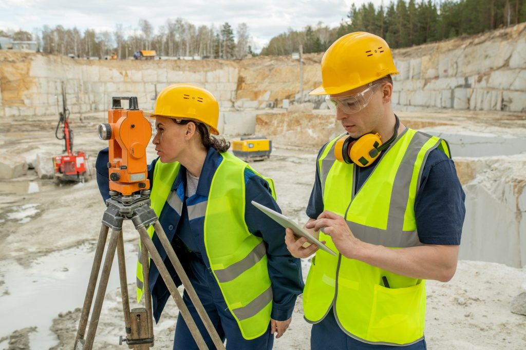 Female engineer using geodetic station by her colleague